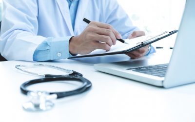 Doctor working with laptop computer and writing on paperwork. Hospital background.